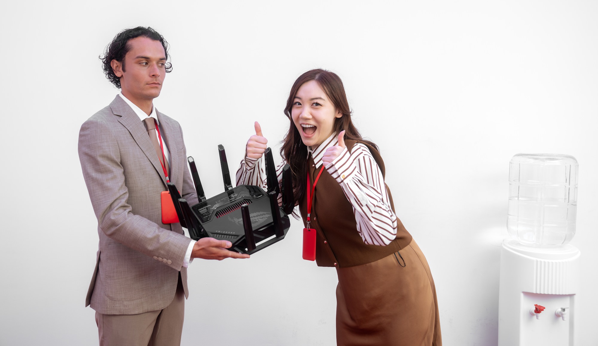 Một người đàn ông và một người phụ nữ đứng bên một máy làm mát nước, người đàn ông cầm bộ định tuyến không dây trong khi người phụ nữ cho một hai ngón tay cái nhiệt tình lên