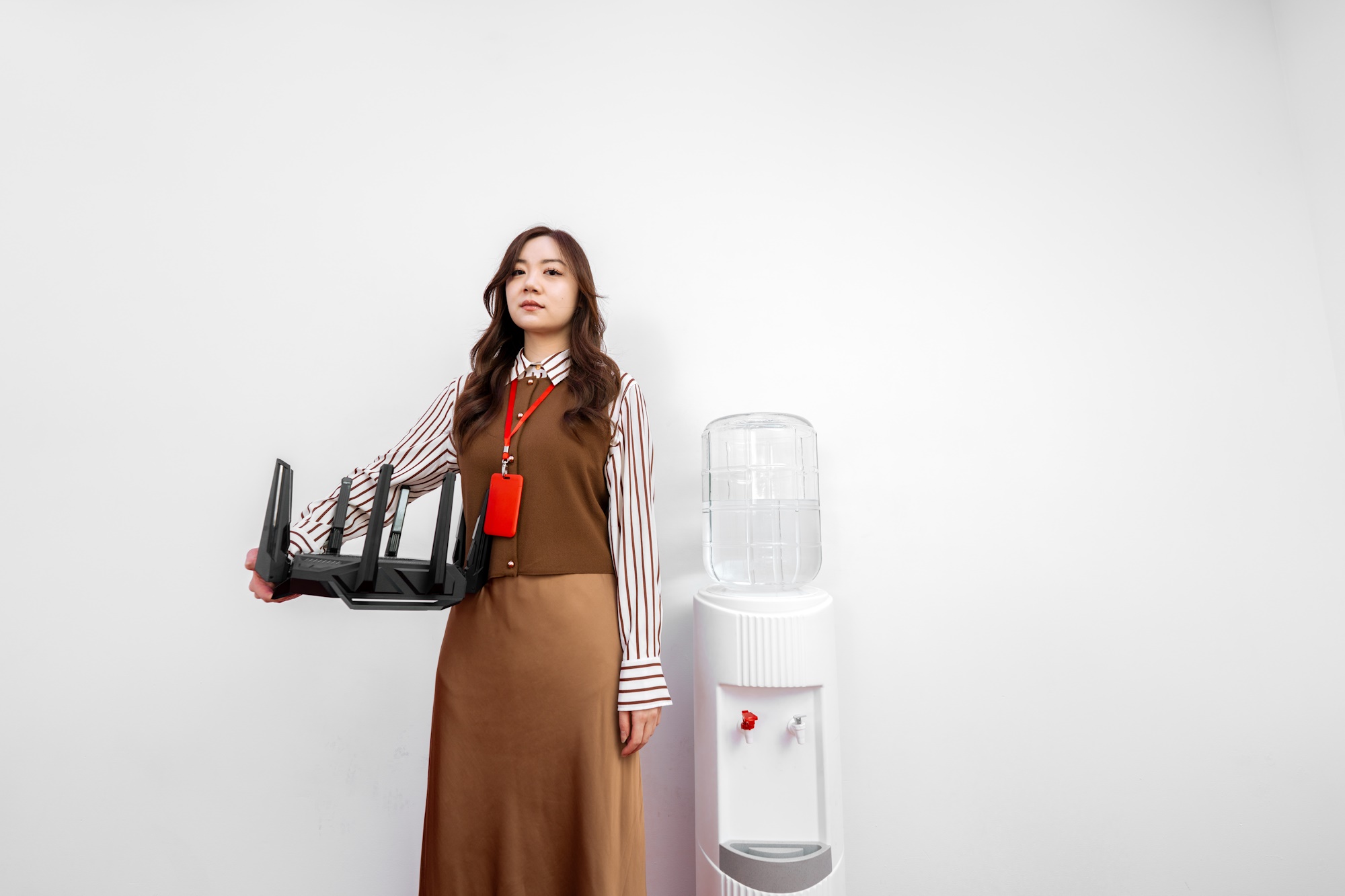 Một phụ nữ trẻ đứng bên một bộ làm mát nước, cầm bộ định tuyến không dây Rog Rapture GT-BE98 Pro bằng một tay